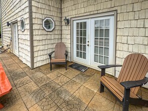 A patio with two Adirondack chairs, a red table, and a house with shingled siding and a white door with glass panels. - Arrant Ridge - Long Range Mountain Views | Pet Friendly | Hot Tub | Firepit | Game Room (Blairsville)