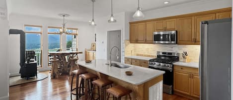 A modern kitchen with a central island, wooden cabinets, stainless steel appliances, and a large window overlooking a scenic view.