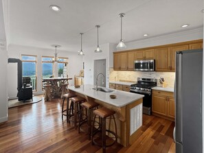 A modern kitchen with a central island, wooden cabinets, stainless steel appliances, and a large window overlooking a scenic view. - Arrant Ridge - Long Range Mountain Views | Pet Friendly | Hot Tub | Firepit | Game Room (Blairsville)