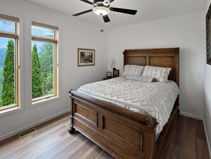 A bedroom with a wooden bed, two windows, a ceiling fan, and a framed picture on the wall. - Arrant Ridge - Long Range Mountain Views | Pet Friendly | Hot Tub | Firepit | Game Room (Blairsville)