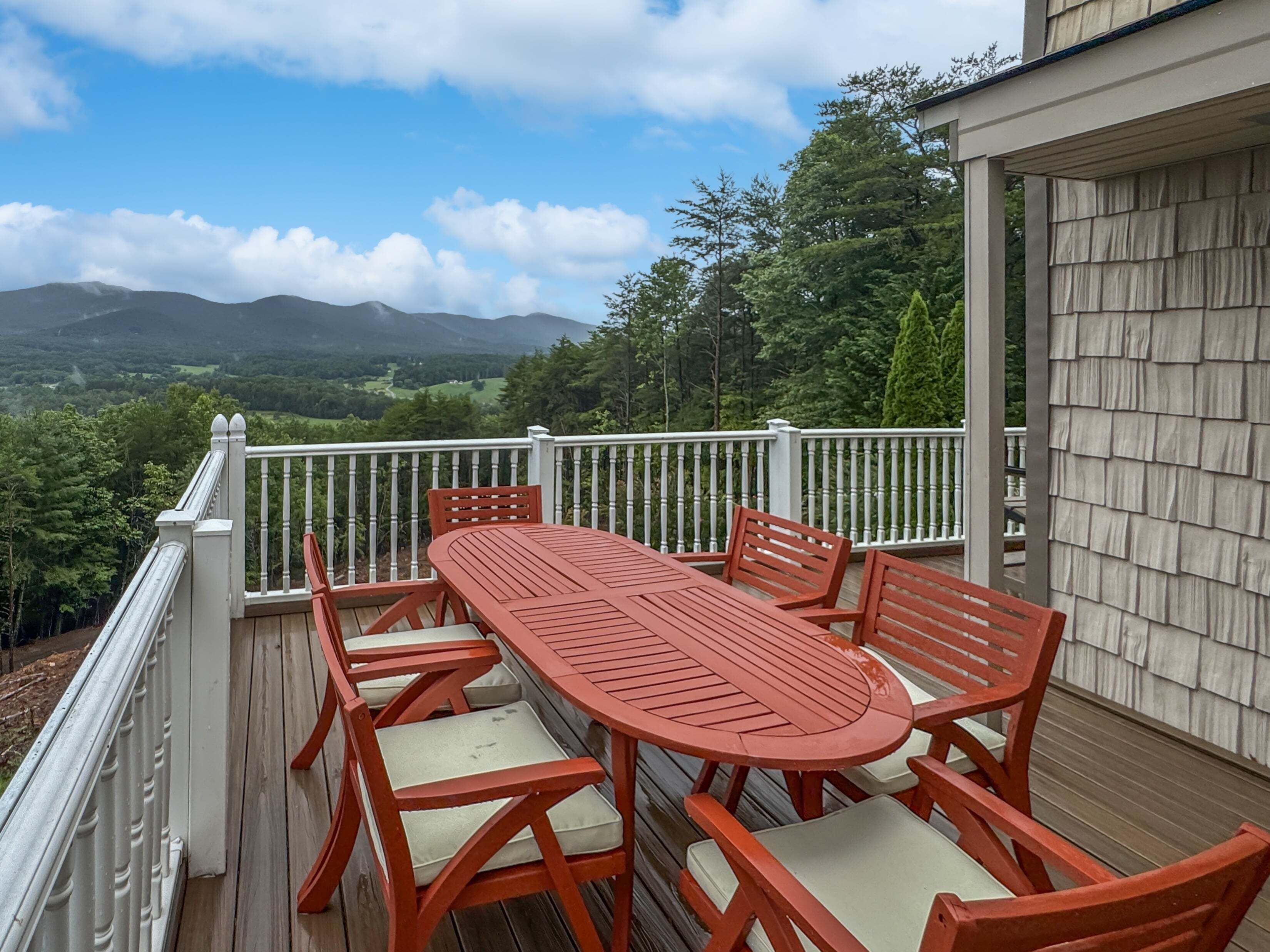 A deck with a table and chairs, overlooking a mountainous landscape.