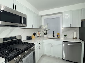 A modern kitchen with white cabinetry, stainless steel appliances, and a window with blinds. - Full Home + Fast Wi-Fi + Washer & Dryer (Park Forest)
