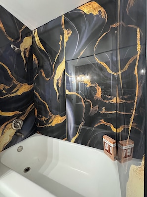 A bathroom with a white bathtub, a black and gold marble wall, and a mirror reflecting the room. - Full Home + Fast Wi-Fi + Washer & Dryer (Park Forest)