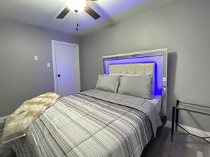A bedroom with a bed, a ceiling fan, a door, and a nightstand. - Full Home + Fast Wi-Fi + Washer & Dryer (Park Forest)
