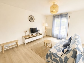 A modern living room with a sofa, a TV, a lamp, and a window with curtains. - Les Glaieuls by Interhome (Deauville-Trouville)