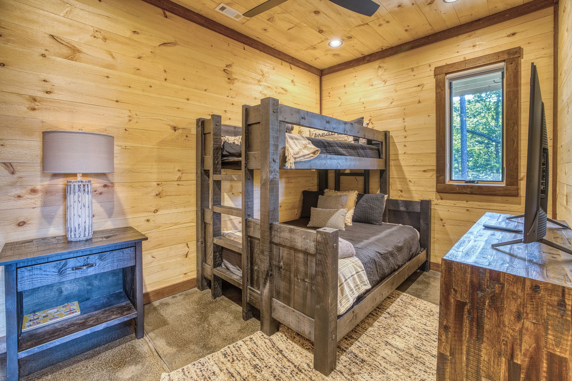 Un lit superposé avec un bureau et une lampe, des murs en bois et une fenêtre.