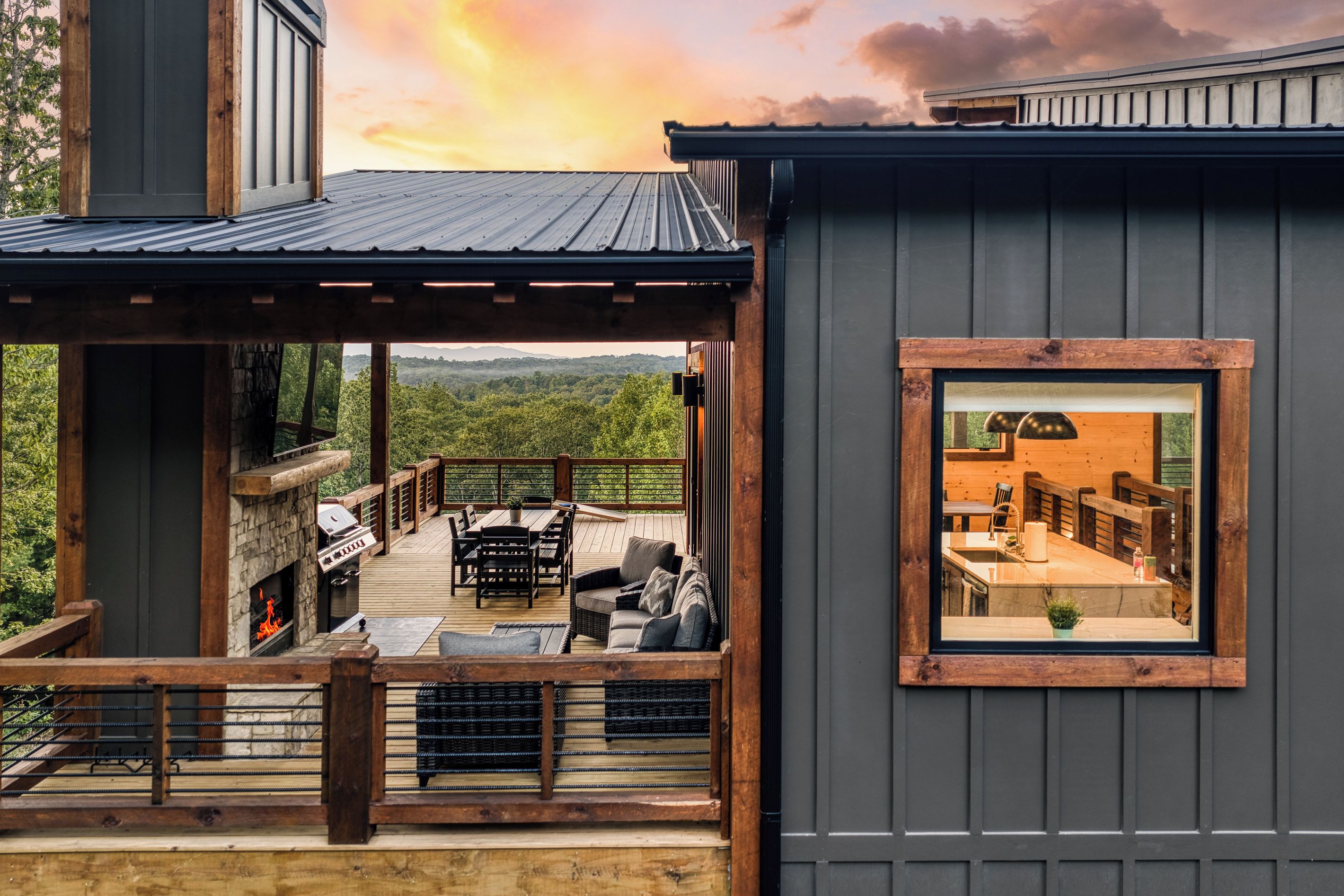Una terraza moderna al aire libre con chimenea de piedra, mobiliario de madera y vista a un paisaje boscoso.