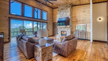 A spacious living room with a stone fireplace, leather sofas, and a large TV mounted on the wall.
