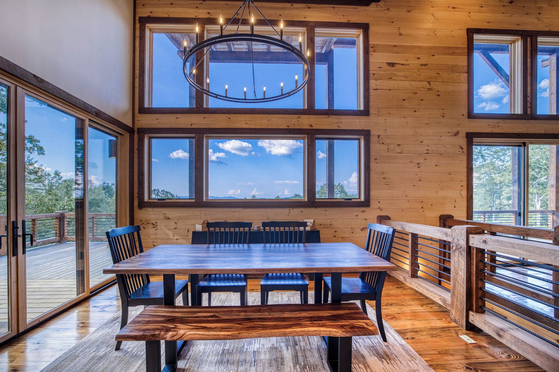 Un espace repas avec une table et des chaises en bois, de grandes fenêtres et un lustre.