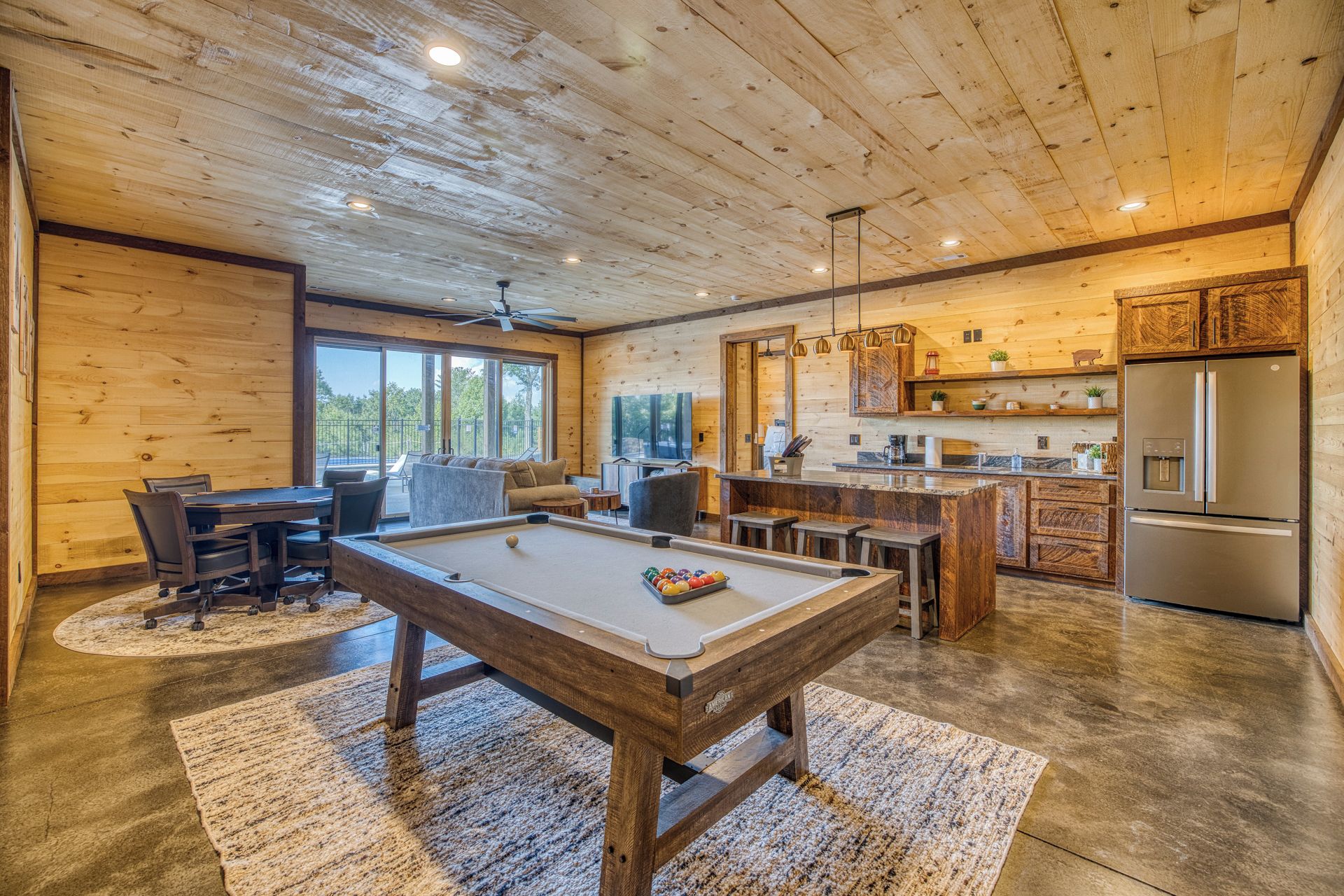 A wooden interior with a pool table, seating area, and kitchen.