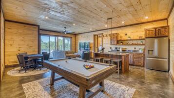 A wooden interior with a pool table, seating area, and kitchen.