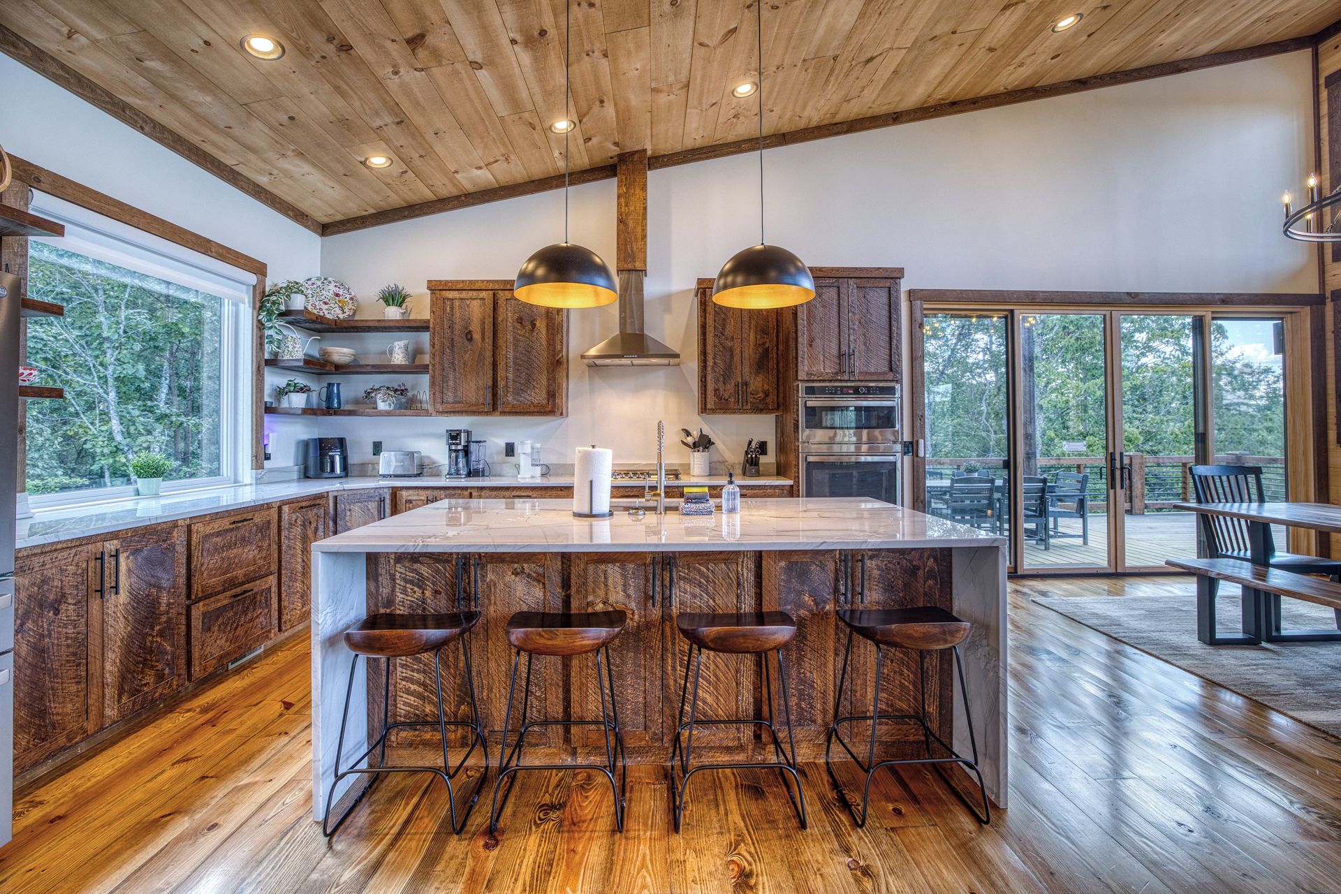 A modern kitchen with wooden cabinets, a large island with bar stools, and a view of the outdoors.