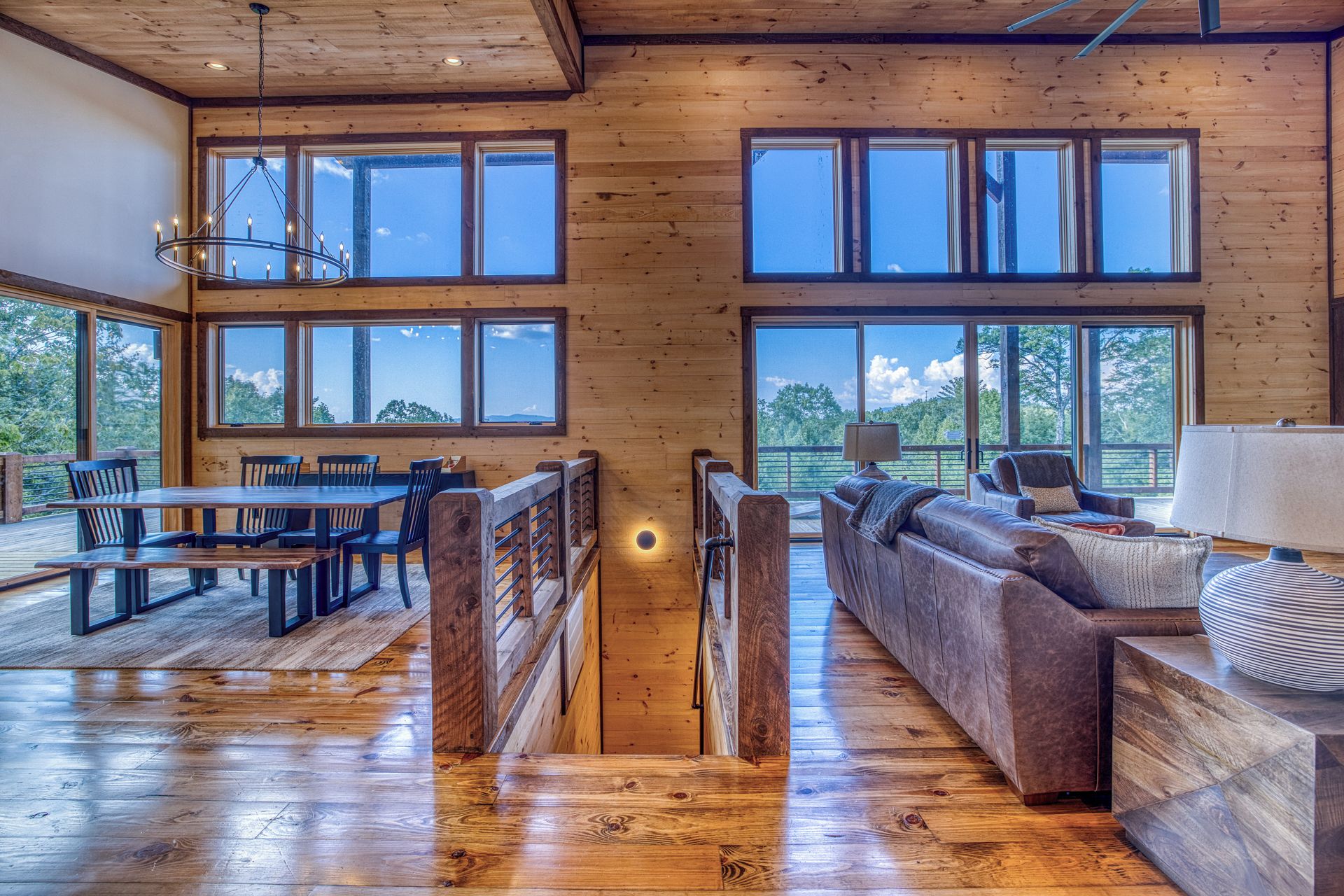 Un vaste espace de vie doté d’un plancher en bois, de grandes fenêtres, d’une table à manger avec des chaises, d’un canapé et d’une lampe.