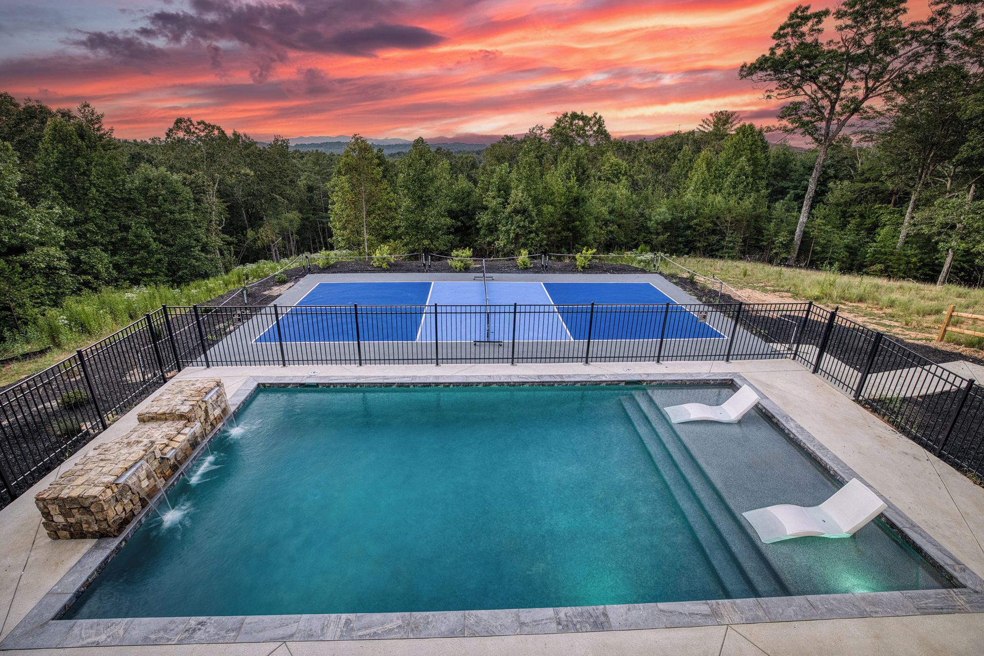 A swimming pool with a surrounding deck and a tennis court.