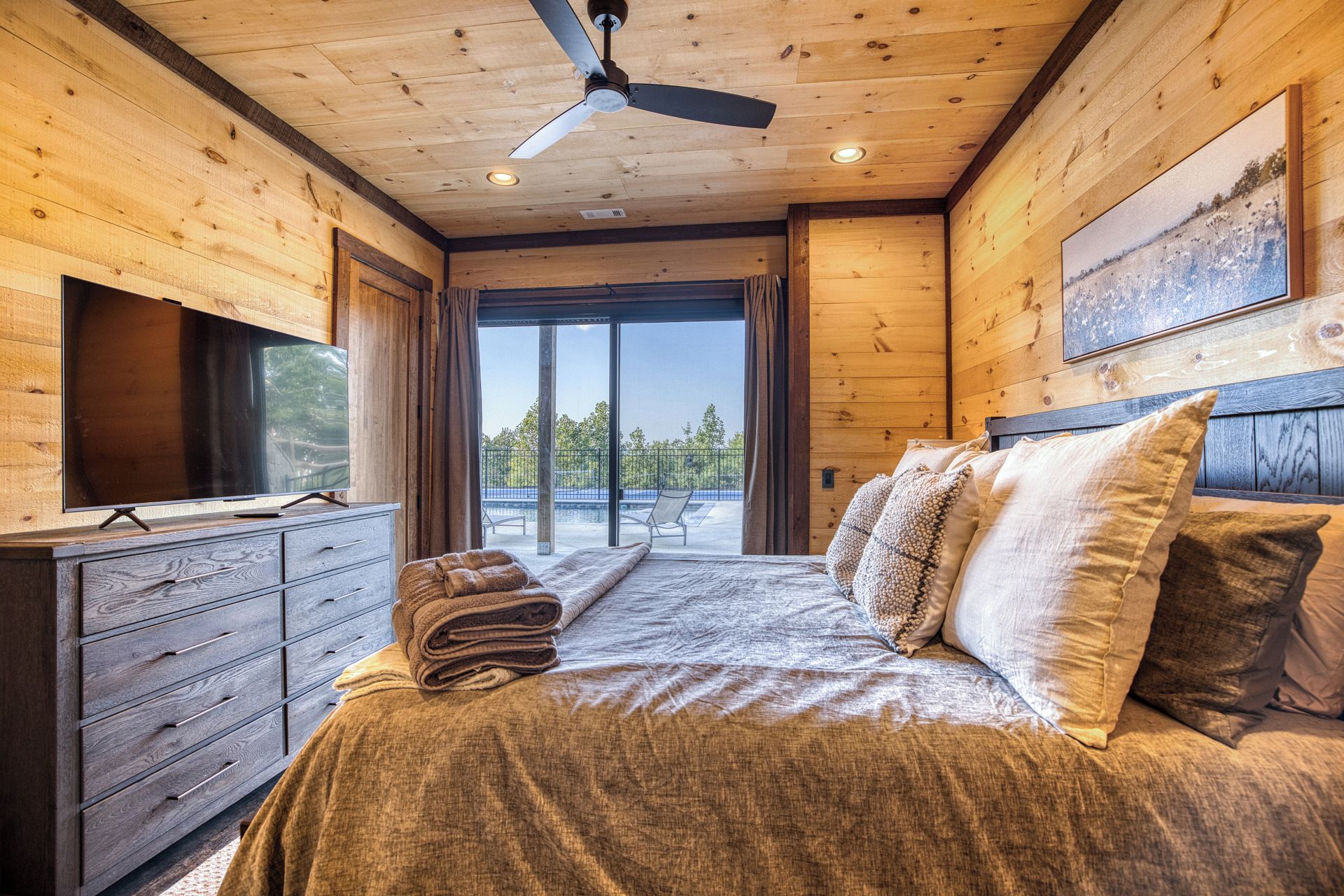 A wooden cabin bedroom with a bed, a television, and a ceiling fan.