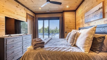 A wooden cabin bedroom with a bed, a television, and a ceiling fan.