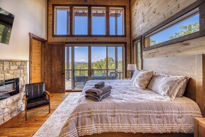 A bedroom with a large bed, a stone fireplace, a wooden ceiling, and a view of the outdoors. - Pickleball Court, Heated Pool, Mtn Views, luxury finishes, close to town (Blue Ridge)