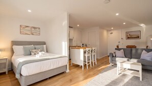 Ein modernes Schlafzimmer mit einem Bett, Nachttischen, einer kleinen Sitzecke mit einer Couch und einem Couchtisch sowie einer Küchenzeile.