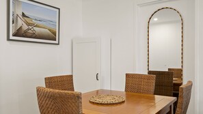 A dining area with a wooden table, wicker chairs, a framed beach photograph, and a large mirror with a colorful border. - Newland Heights Rooftop Pool & Bondi Living (Bondi Junction)