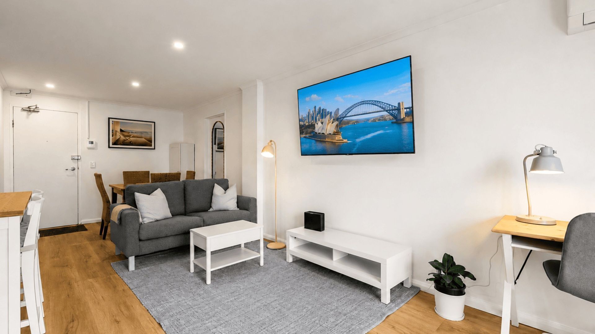 Un salon moderne avec un canapé gris, une table basse blanche et un téléviseur à écran plat fixé au mur.