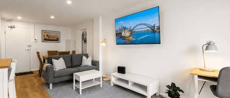 Una sala de estar moderna con un sofá gris, una mesa de centro blanca y un televisor de pantalla plana montado en la pared.
