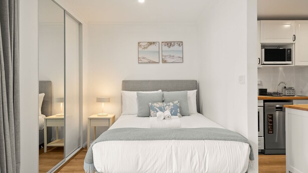 Ein modernes Schlafzimmer mit Bett, Nachttischen und Blick in den angrenzenden Küchenbereich.