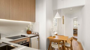 A modern kitchen with a built-in oven, a sink, and a dining area with a wooden table and chairs. - The Plot Twist Randwick Unit 2 (Randwick)