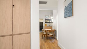 A hallway with a wooden wardrobe, a dining area with a table and chairs, and a wall-mounted artwork. - The Plot Twist Randwick Unit 2 (Randwick)