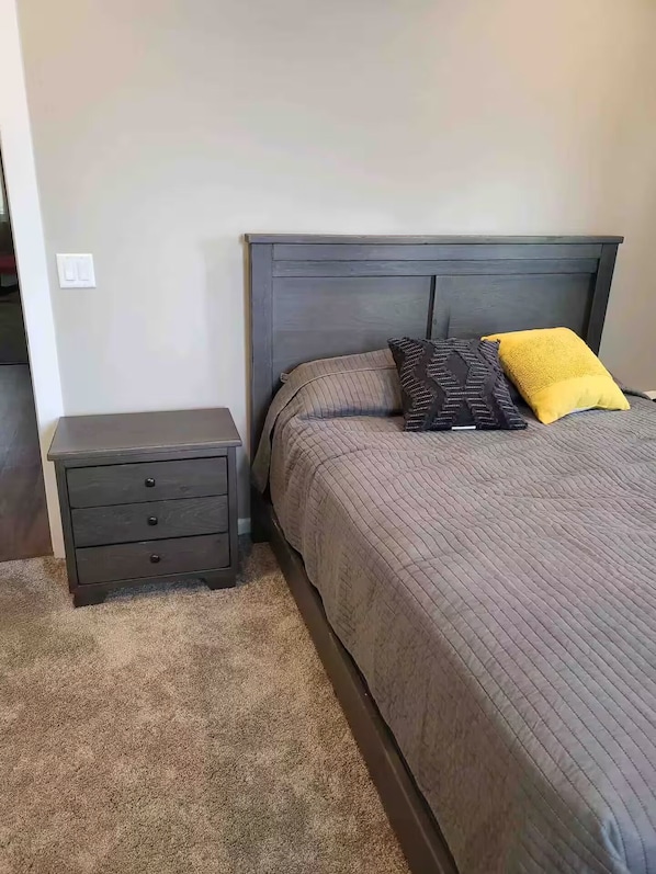Une chambre à coucher avec un lit, une table de chevet et un sol recouvert d’une moquette.