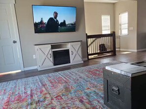Ein Wohnzimmer mit Kamin, einem darüber montierten Fernseher, einem gemusterten Teppich und einer Holzbank.