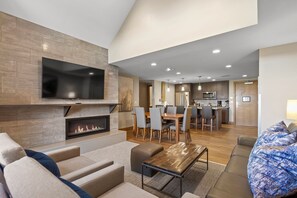 A modern living room with a fireplace, a flat-screen TV, and a dining area with a kitchen in the background. - Grand Colorado Peak 8 | Spacious 4-Bedroom (Two Full 2-Bedroom Villas) (Breckenridge)