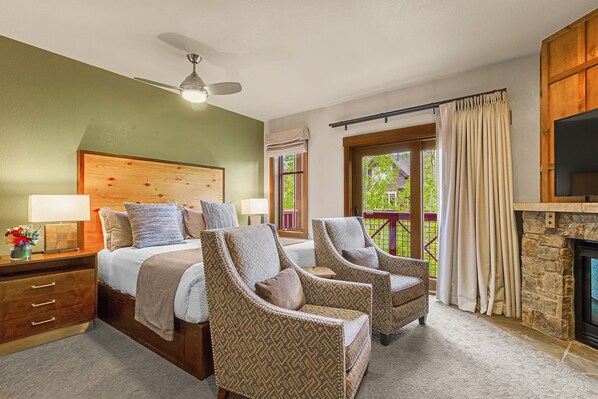 Une chambre à coucher comprenant un lit, deux fauteuils, une table de chevet, une lampe, un ventilateur de plafond, une fenêtre avec des rideaux et une cheminée.