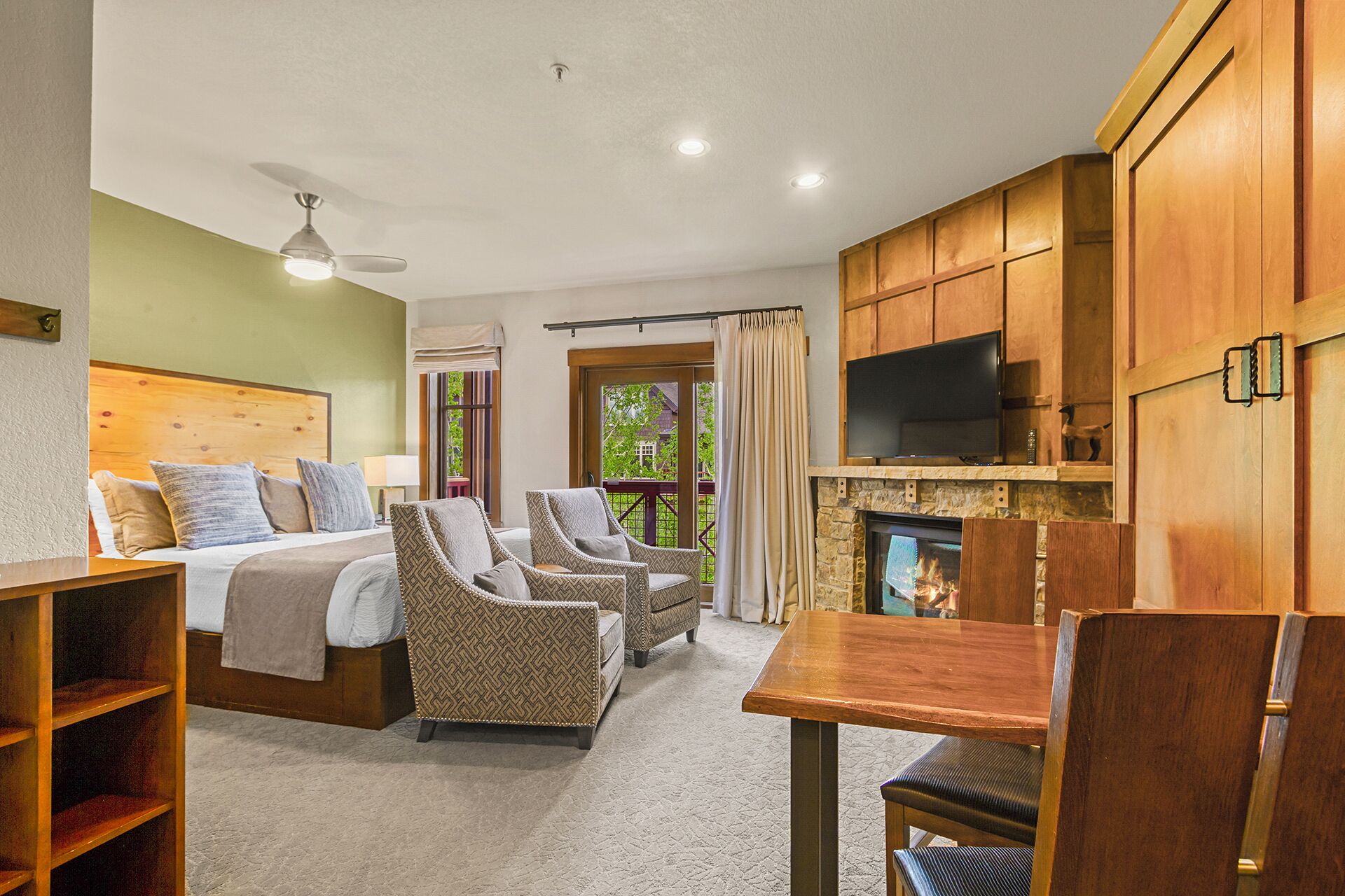 Une chambre d’hôtel avec un lit, deux fauteuils, une table en bois, une télévision et une cheminée.
