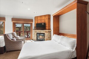 A bedroom with a large bed, a fireplace, a TV, and a balcony with chairs. - Hyatt Main St Studio | Steps to Peak 9 + Downtown (Breckenridge)