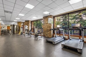 Une salle de sport équipée de tapis de course, d’appareils de musculation et d’un mur en pierre.