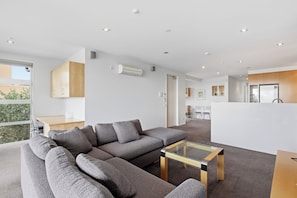 Ein modernes Wohnzimmer mit einem Ecksofa, einem Glastisch und Blick ins Freie.
