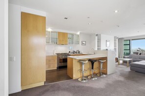 A modern kitchen with a central island, bar stools, and a dining area with a sofa and table. - Penthouse Apartment in the heart of Nelson (Nelson)
