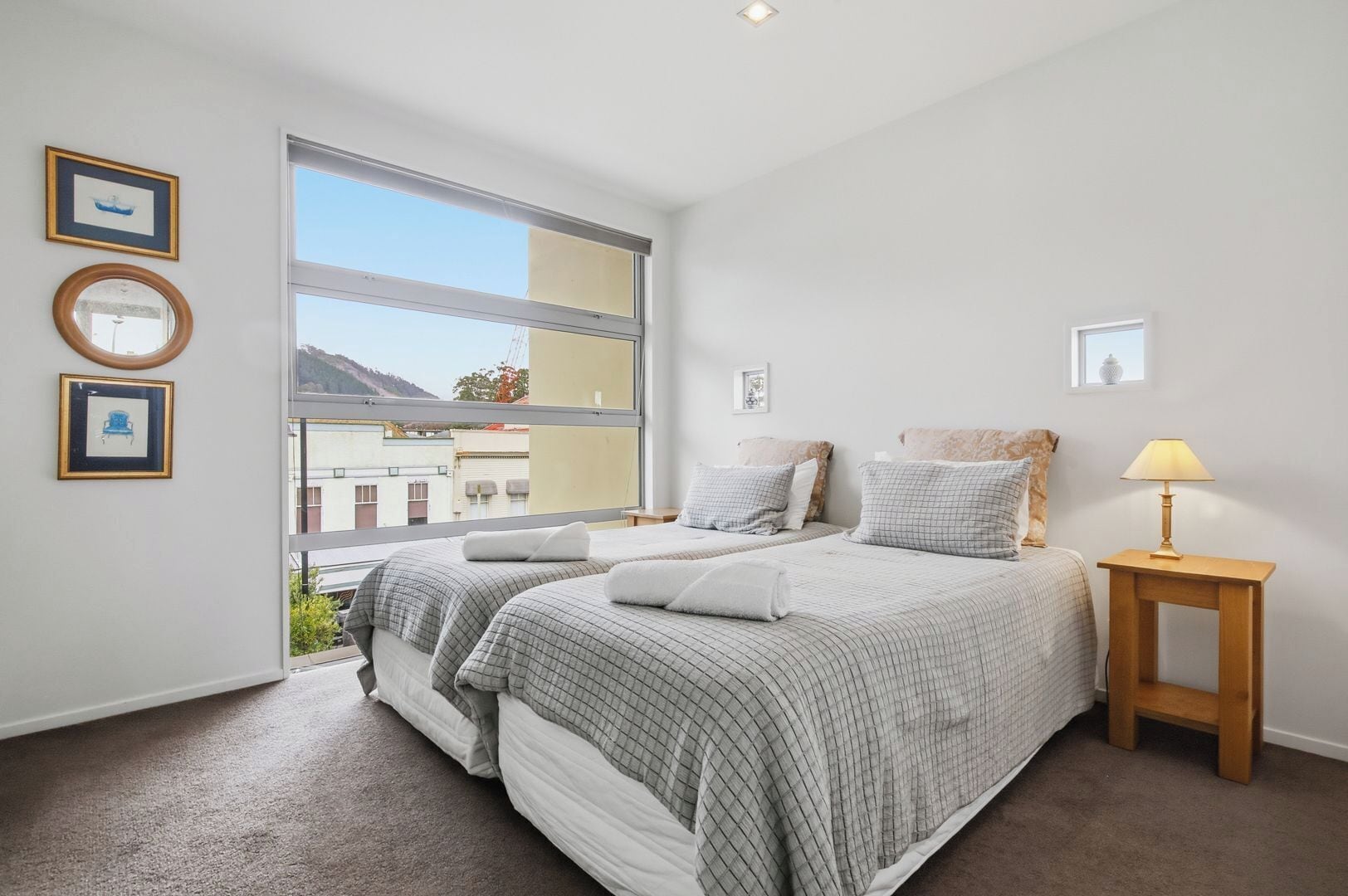A bedroom with two beds, a window, and a bedside table with a lamp.