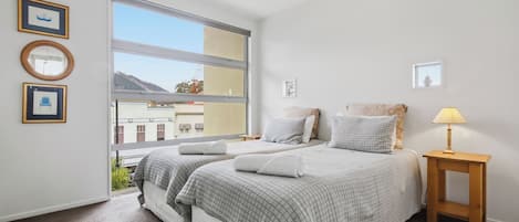 A bedroom with two beds, a window, and a bedside table with a lamp.