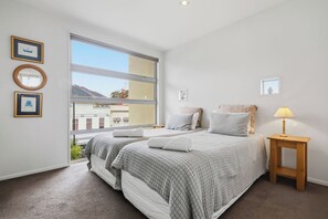A bedroom with two beds, a window, and a bedside table with a lamp. - Penthouse Apartment in the heart of Nelson (Nelson)