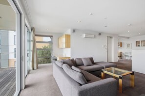 A modern living room with a sectional sofa, a glass coffee table, and a view of a balcony. - Penthouse Apartment in the heart of Nelson (Nelson)