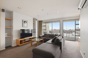 Ein modernes Wohnzimmer mit Flachbildfernseher, einer Couch, einem Couchtisch und Blick auf die Stadt durch große Fenster.