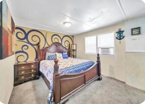 Quarto com cama de madeira, mesa de cabeceira, cômoda e parede com padrão decorativo.