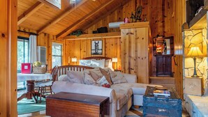 Interior acogedor de una cabaña con techo de madera, cama, escritorio con lámpara y chimenea.