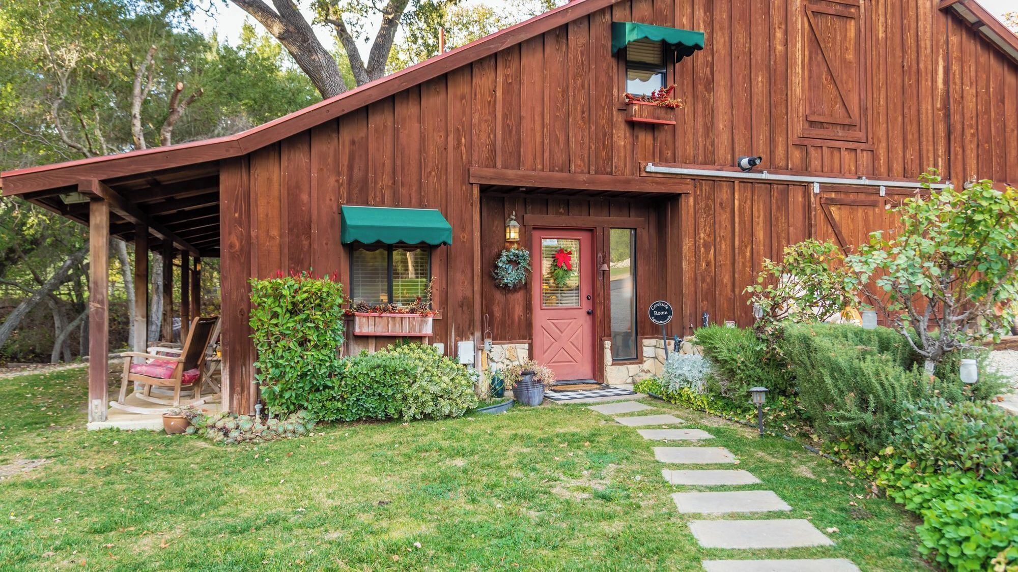 A rustic wooden barn with a porch, a red door, and a sign indicating a room for sale.