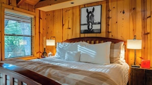 Habitación con paneles de madera, una cama, dos lámparas de noche, un cuadro en la pared y una ventana con persianas.