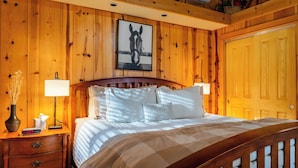 Habitación con paneles de madera, una cama, lámparas de noche, un reloj y un cuadro en la pared.