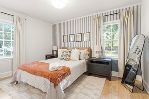 Un dormitorio con cama, mesitas de noche, espejo y ventana con cortinas.