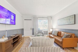 A living room with a flat-screen TV, a sofa, a striped armchair, a wooden cabinet, and a painting on the wall. - Peaceful 2bed /1 bath corporate duplex Powder Springs - Cobb county pet friendly (Powder Springs)