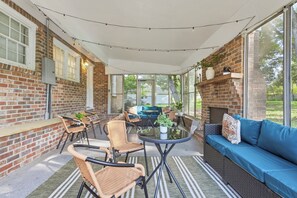 Ein Terrassenbereich im Freien mit Ziegelmauern, einem blauen Sofa, Korbstühlen und einem Tisch mit Glasplatte.